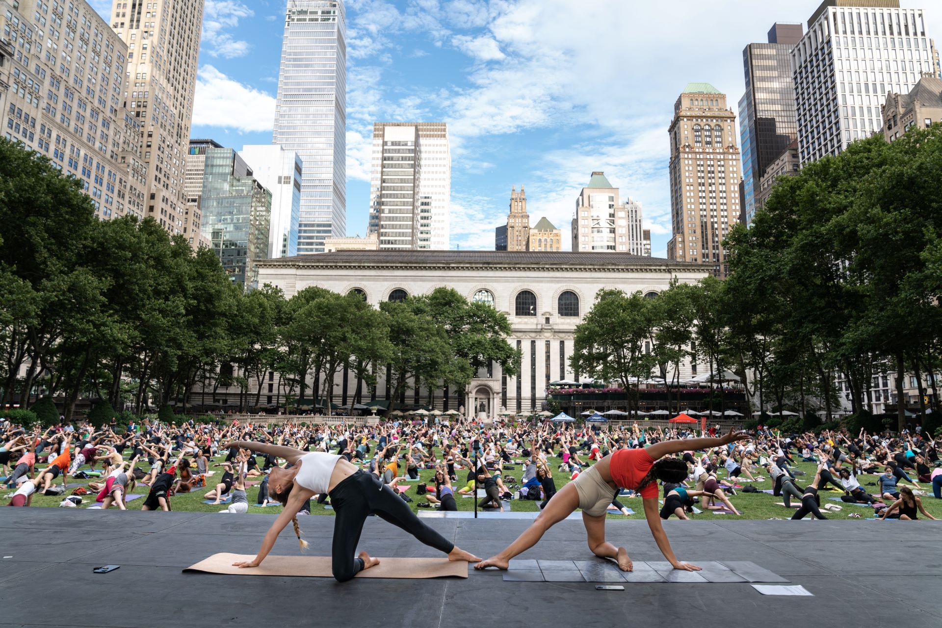 Two instructors guiding over 1,000 yogis through a yoga pose on Bryant Park's lawn.
