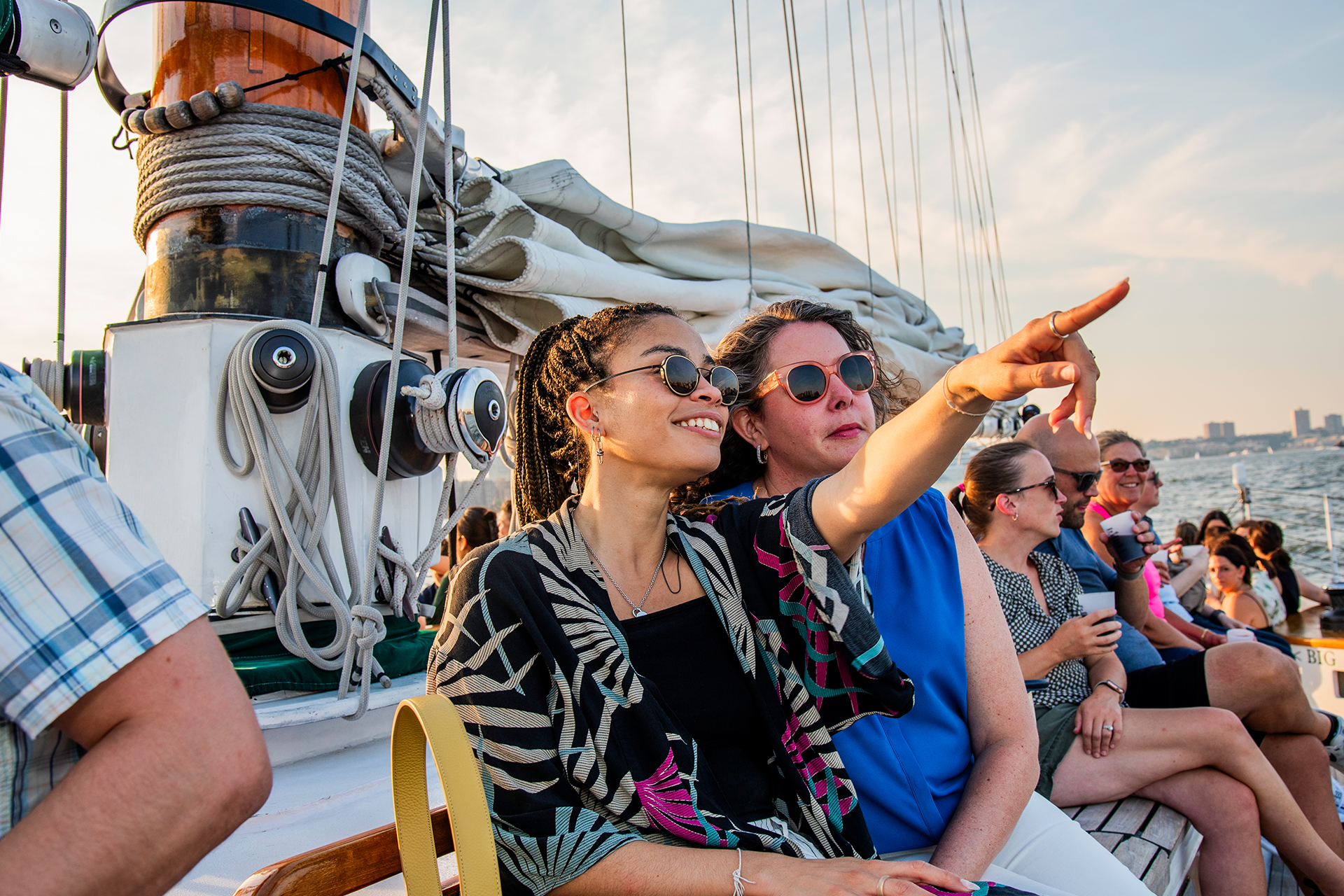 Two women sitting on a schooner in NY Harbor pointing out at something.