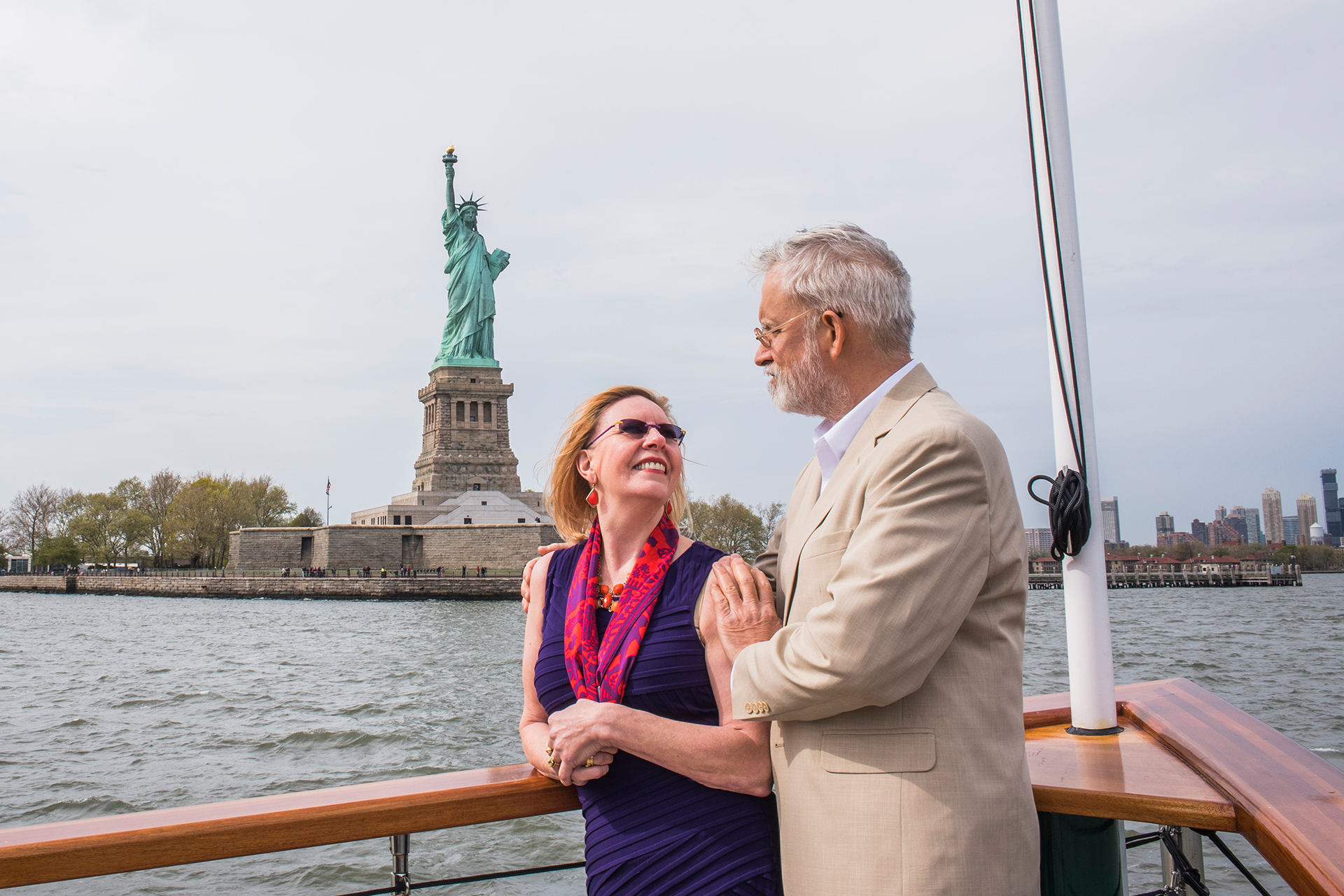 Couple on the bow of a Classic Harbor Line yacht with the Statue of LIberty in the background.