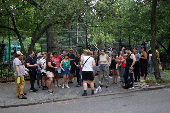 Group of people stands on sidewalk in front of a tour guide.