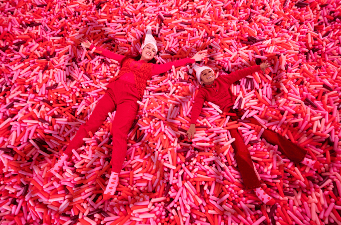 Mother and child smiling while laying atop endless giant sprinkles, dressed in holiday pajamas.