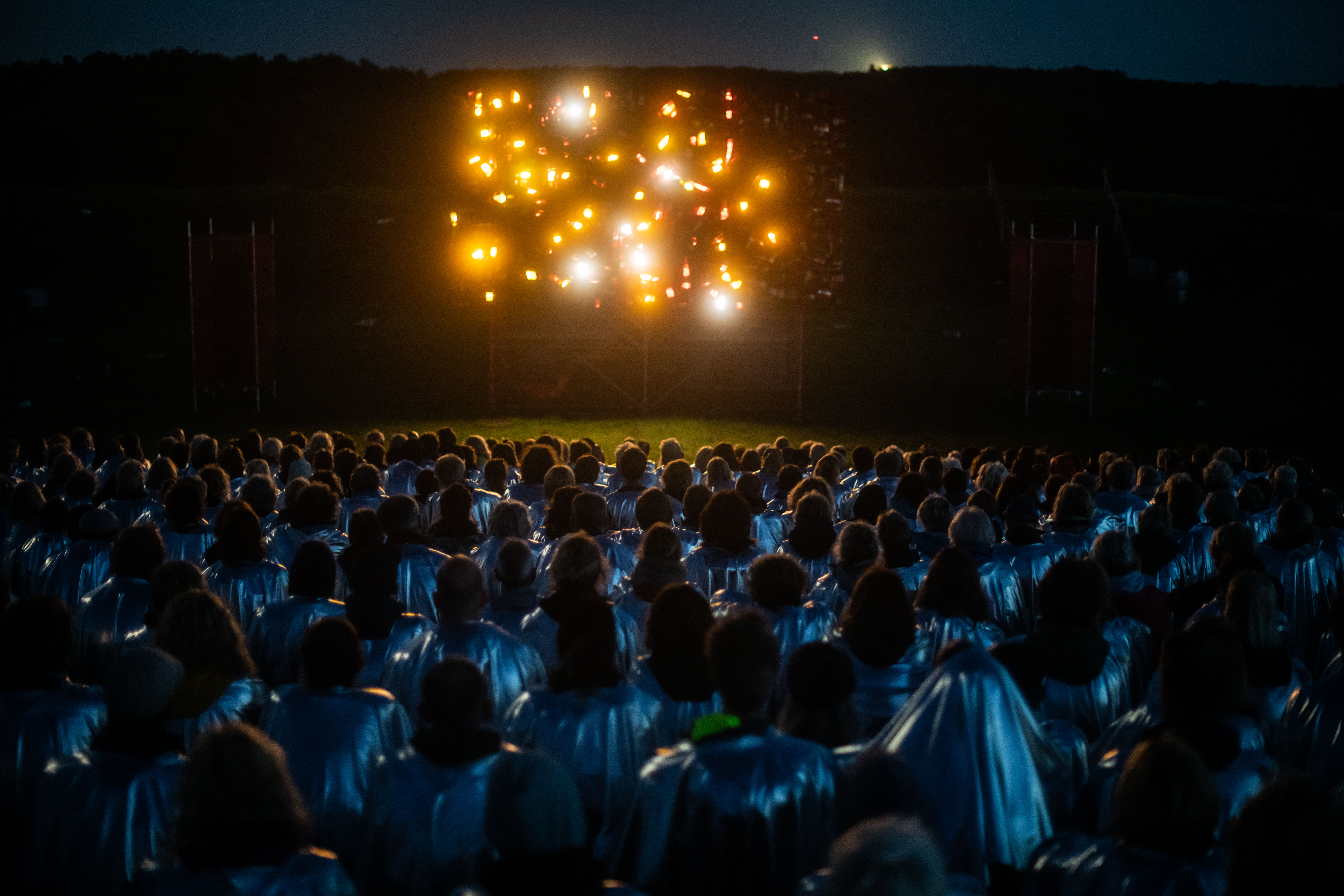 Photo of large structure made from car taillights with audience members in metallic grey cloaks visible in the foreground.