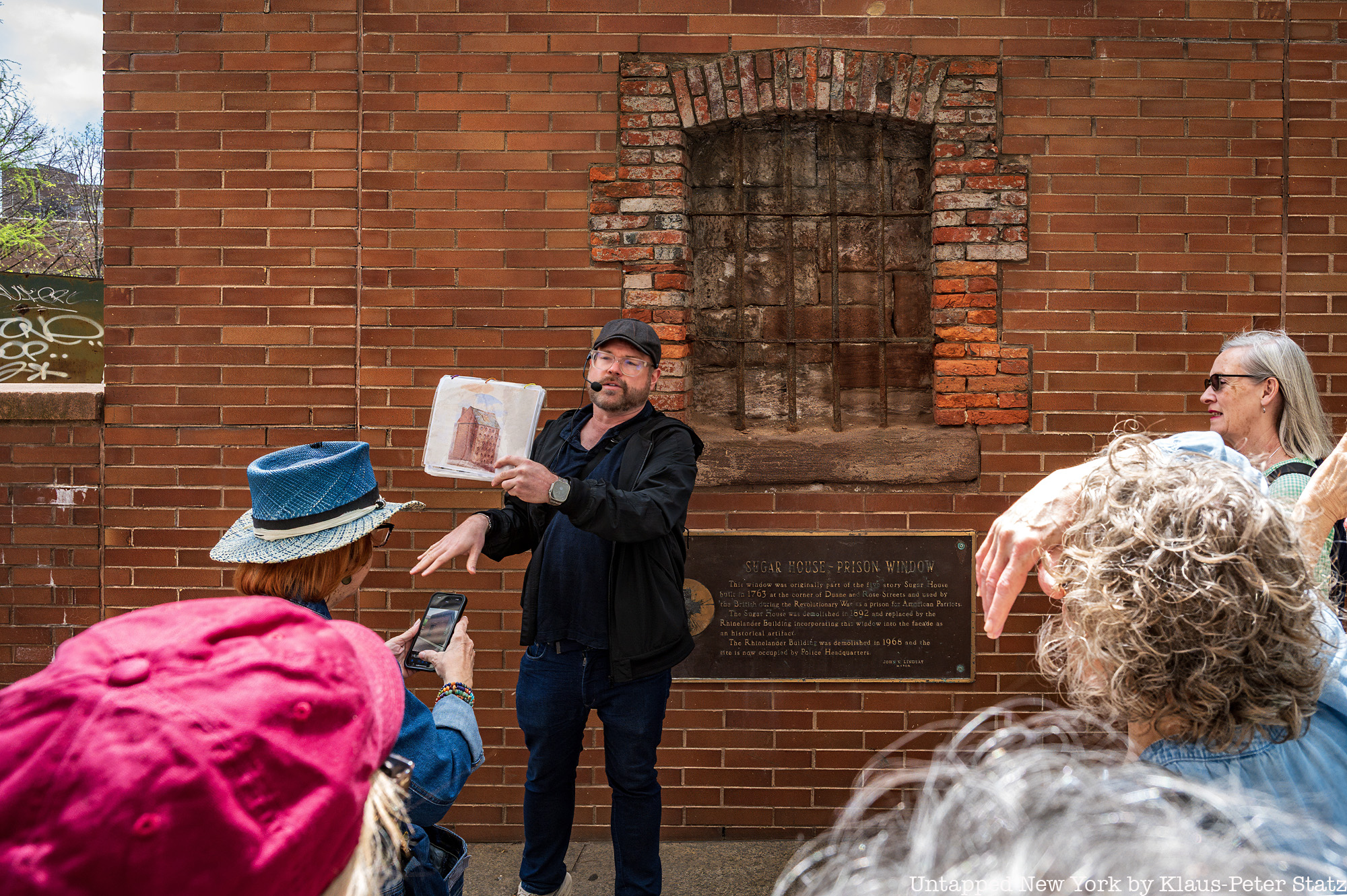 Guide pointing to the Sugar House Prison Window, a surviving remnant of the Revolutionary War in Lower Manhattan, during an Untapped New York walking tour.